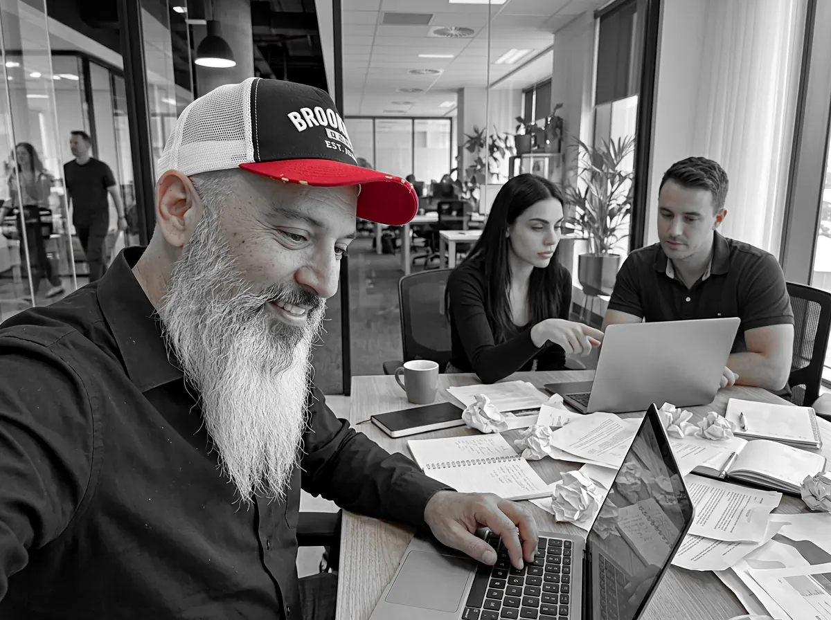 Shai Agiv smiling at his laptop during a creative session while two clients work on their ads